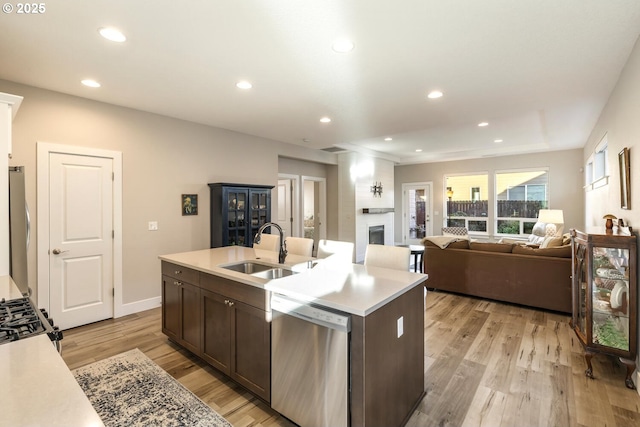 kitchen with a fireplace, stainless steel appliances, light countertops, a sink, and light wood-type flooring