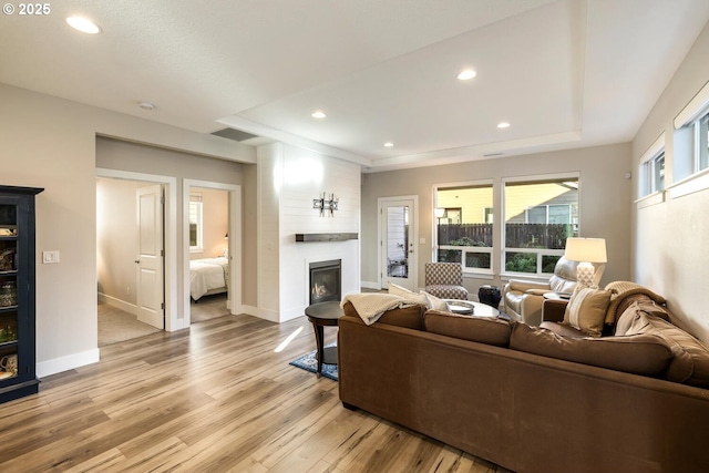 living room featuring a tray ceiling, light wood-style flooring, baseboards, and recessed lighting