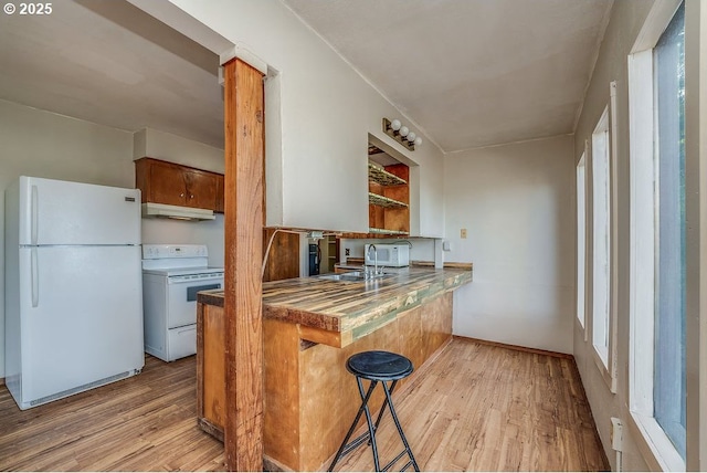 kitchen featuring white appliances, kitchen peninsula, light hardwood / wood-style floors, a breakfast bar, and sink