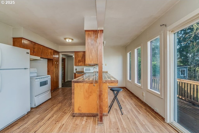 kitchen with white appliances, kitchen peninsula, light hardwood / wood-style flooring, a kitchen bar, and sink