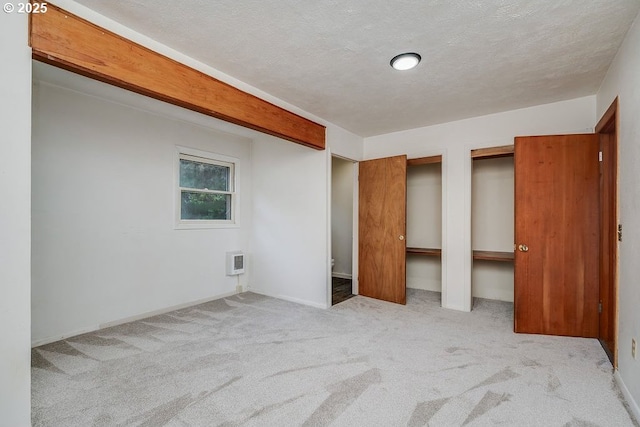 unfurnished bedroom featuring a textured ceiling, light colored carpet, and multiple closets