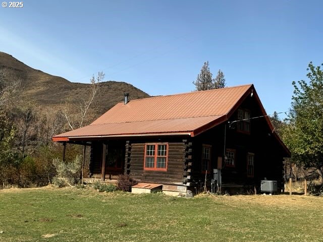 rear view of house with a lawn, log exterior, metal roof, central air condition unit, and a mountain view