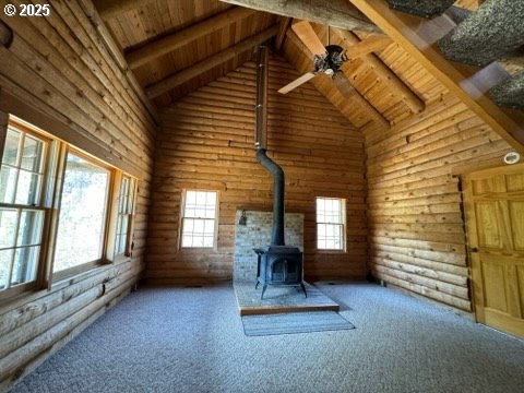 unfurnished living room featuring wood ceiling, beamed ceiling, carpet flooring, and a wood stove