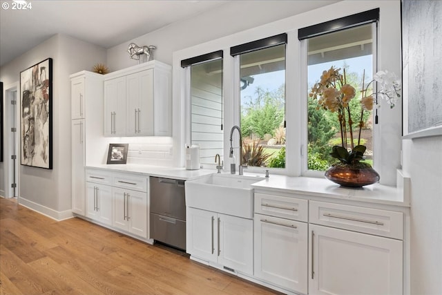 kitchen featuring stainless steel dishwasher, light countertops, light wood-style floors, and white cabinetry