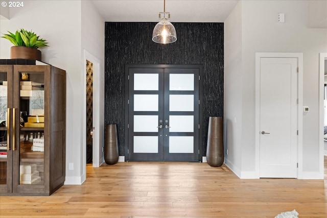 foyer with baseboards, french doors, an accent wall, and light wood-style floors