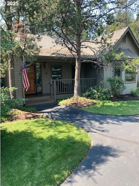 view of front of property with a porch, a front yard, and a shingled roof