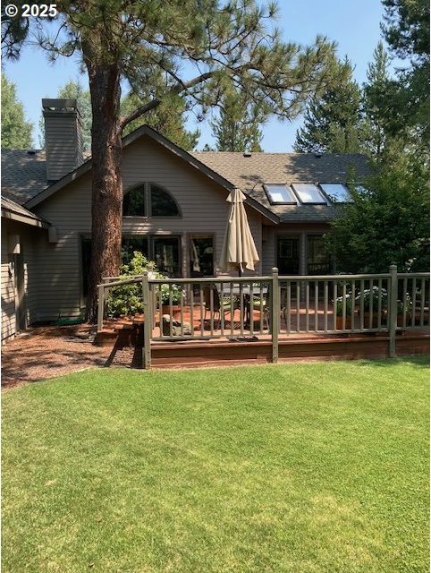 back of property with a lawn, a chimney, and a deck