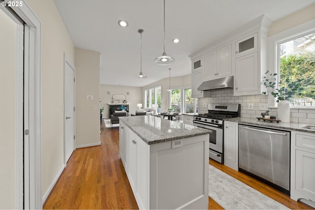 kitchen featuring glass insert cabinets, stainless steel appliances, backsplash, under cabinet range hood, and a kitchen island