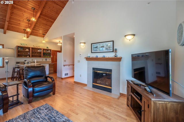 1312 Village Loop, Bandon, OR 97411 - living area featuring a tile fireplace, light wood-style floors, a wooden ceiling with exposed beams, and high vaulted ceiling