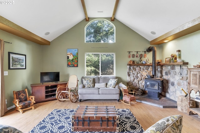 living room featuring wood-type flooring, plenty of natural light, beamed ceiling, and a wood stove