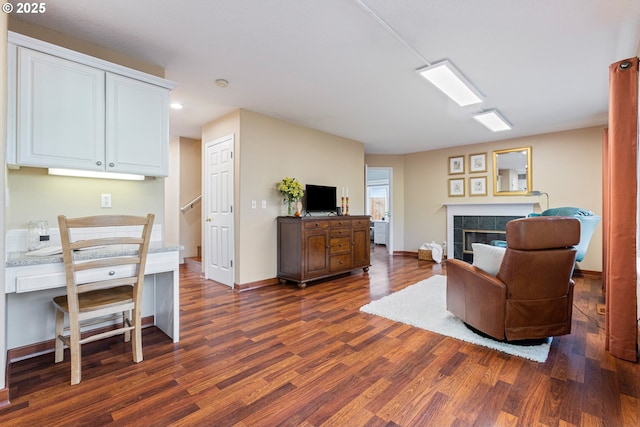 living area featuring baseboards, dark wood-type flooring, stairs, and a tile fireplace