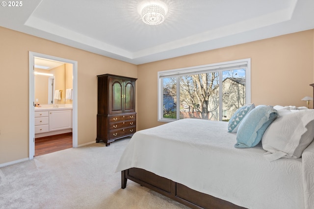 bedroom featuring baseboards, a raised ceiling, light carpet, and connected bathroom