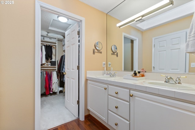 bathroom with double vanity, wood finished floors, a walk in closet, and a sink