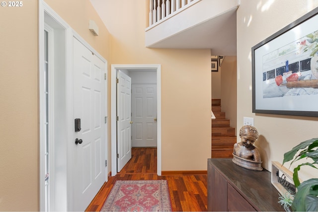 corridor with a high ceiling, stairway, wood finished floors, and baseboards