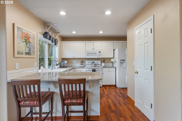 kitchen featuring white appliances, white cabinetry, a peninsula, and a sink