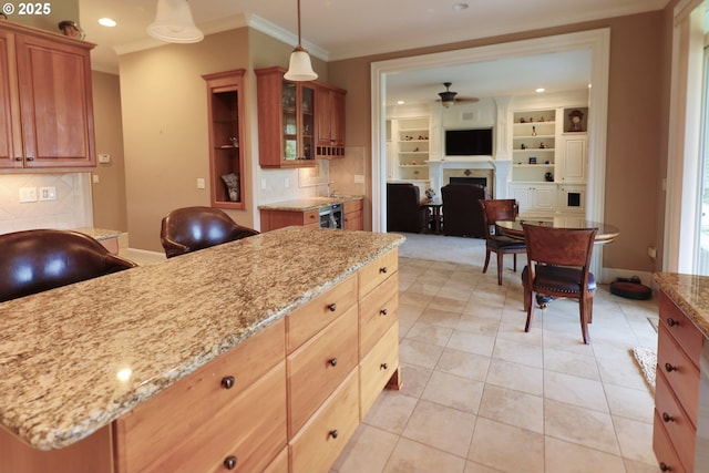 kitchen featuring light stone counters, a fireplace, a ceiling fan, glass insert cabinets, and ornamental molding