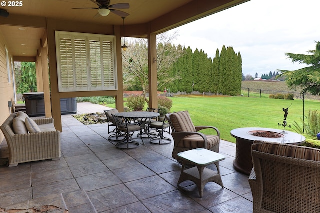 view of patio with ceiling fan, outdoor dining area, a fire pit, fence, and a hot tub