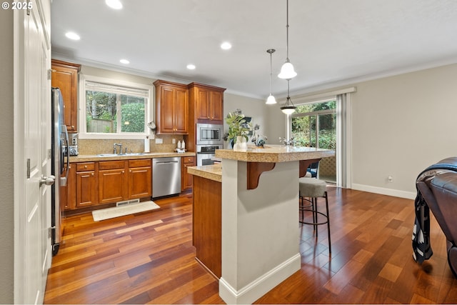 12647 SW 21st Ct, Lake Oswego, OR 97035 - kitchen featuring appliances with stainless steel finishes, crown molding, brown cabinets, light countertops, and a kitchen bar