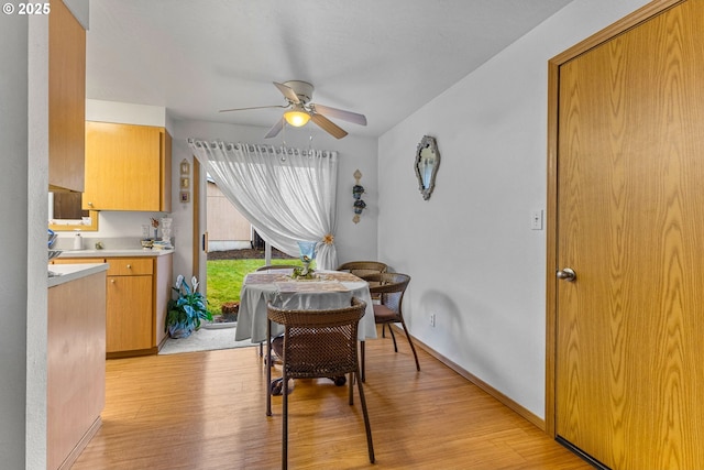 dining space featuring light wood finished floors, a ceiling fan, and baseboards