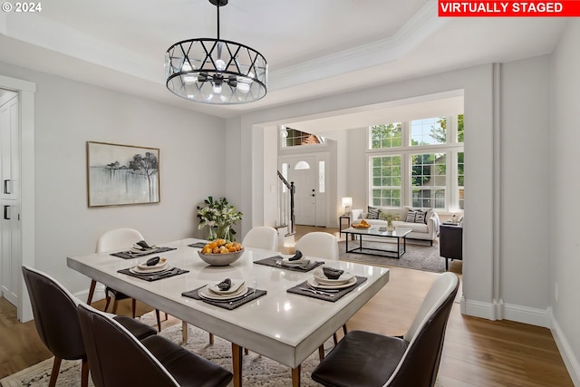 dining space with hardwood / wood-style flooring, a tray ceiling, crown molding, and a notable chandelier