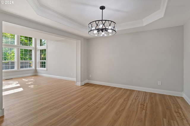 spare room with a tray ceiling, light hardwood / wood-style flooring, ornamental molding, and a chandelier