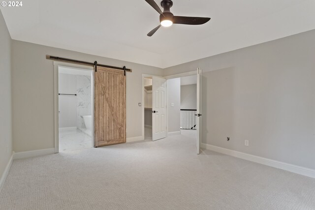 unfurnished bedroom featuring connected bathroom, a spacious closet, a closet, light colored carpet, and a barn door