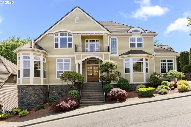 view of front of home featuring a balcony, french doors, stone siding, and a tiled roof