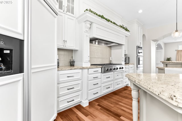 kitchen with appliances with stainless steel finishes, white cabinetry, tasteful backsplash, dark wood-style floors, and arched walkways