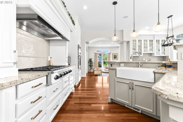 kitchen with premium range hood, a sink, stainless steel gas stovetop, tasteful backsplash, and arched walkways