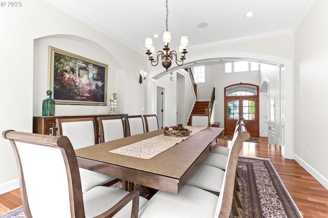 dining room featuring arched walkways, a chandelier, wood finished floors, ornamental molding, and stairs