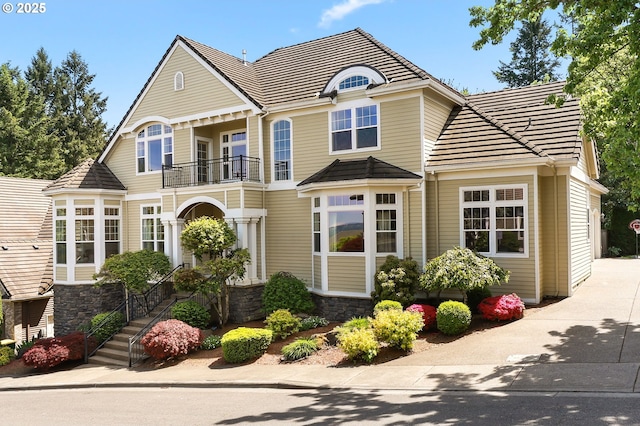 view of front of home with a balcony, driveway, stone siding, and a tiled roof