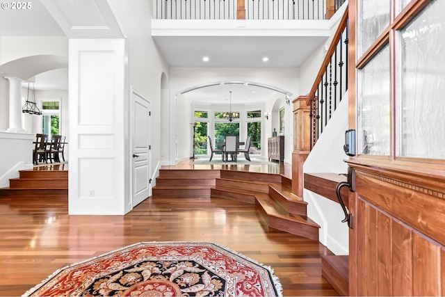 foyer with arched walkways, stairs, wood finished floors, recessed lighting, and a high ceiling