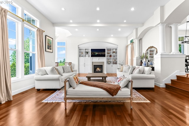 living area featuring wood finished floors, ornate columns, baseboards, a lit fireplace, and recessed lighting
