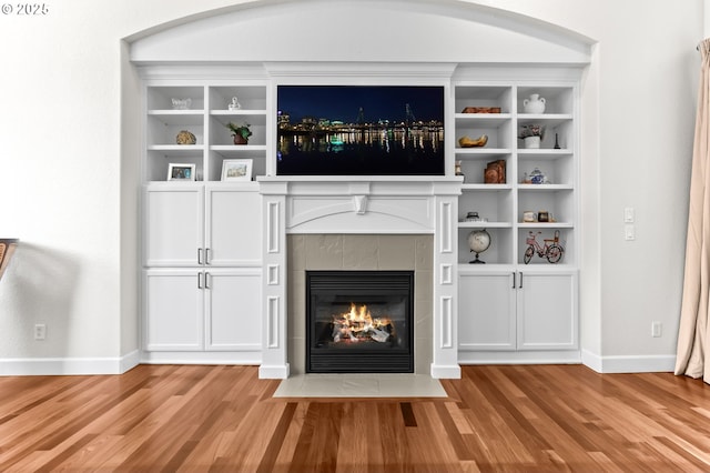 unfurnished living room featuring a tiled fireplace, light wood-type flooring, and baseboards