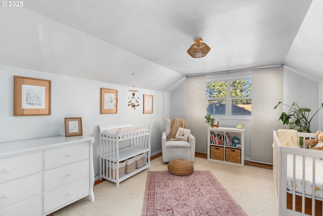 bedroom with lofted ceiling, a crib, and light carpet