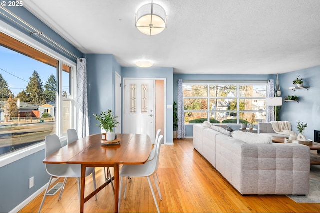 dining space with a textured ceiling, light hardwood / wood-style floors, and a healthy amount of sunlight