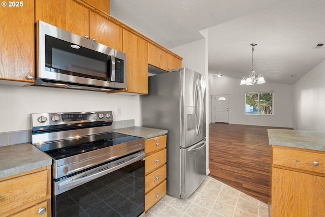 kitchen with pendant lighting, light tile patterned floors, lofted ceiling, appliances with stainless steel finishes, and a notable chandelier