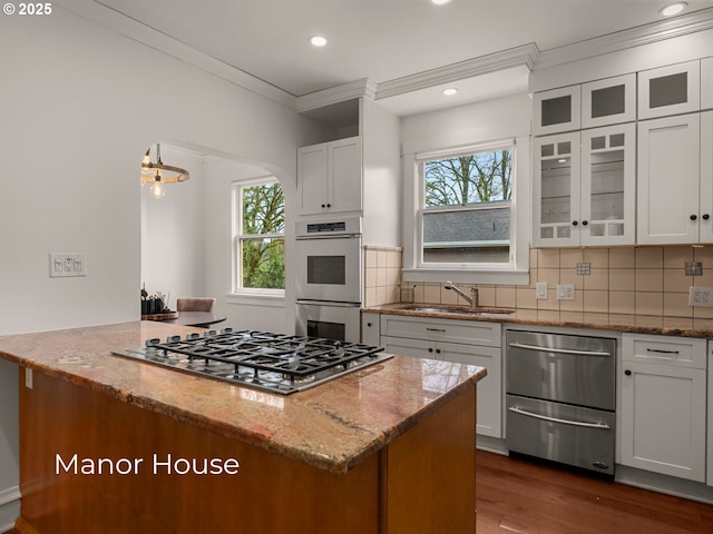 kitchen featuring double wall oven, stainless steel gas stovetop, backsplash, and a sink