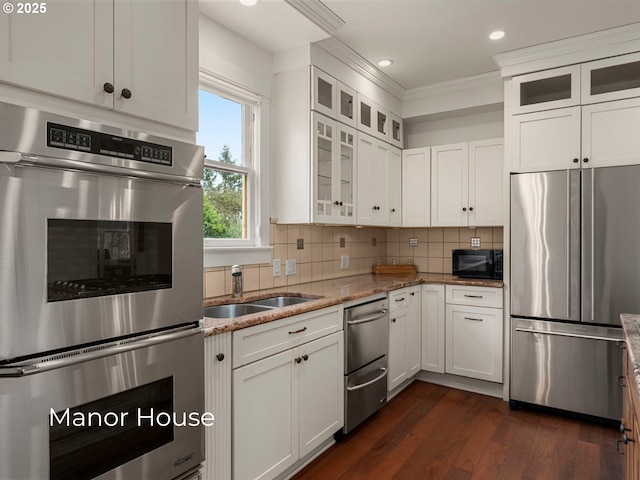 kitchen featuring light stone countertops, a sink, decorative backsplash, white cabinets, and appliances with stainless steel finishes