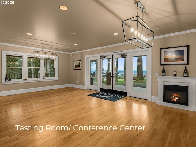 interior space featuring a glass covered fireplace, crown molding, wood finished floors, and french doors