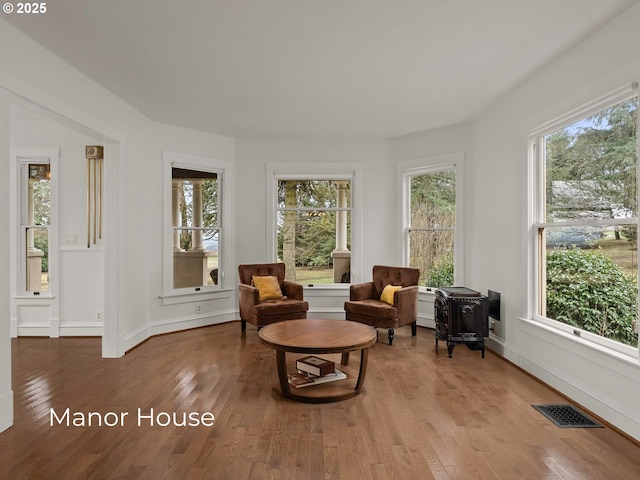 living area with visible vents, a wood stove, baseboards, and hardwood / wood-style flooring