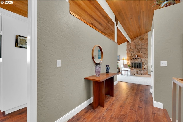 hallway featuring baseboards, a textured wall, wooden ceiling, wood finished floors, and vaulted ceiling with beams