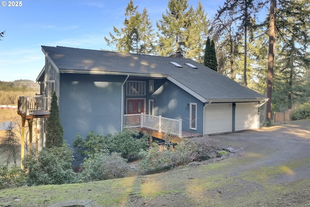 view of front of home with aphalt driveway, roof with shingles, a chimney, and a garage