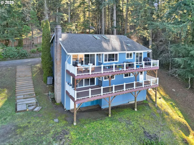 back of house featuring a lawn, a chimney, roof with shingles, a deck, and central AC