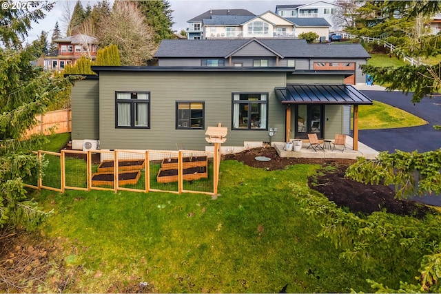 rear view of property featuring a lawn, a standing seam roof, a patio area, fence, and metal roof