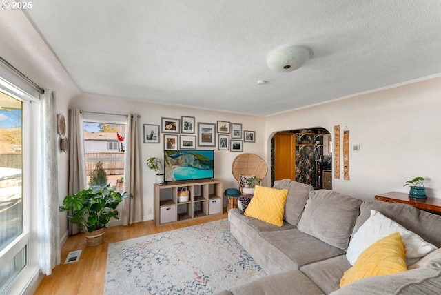 living room featuring arched walkways, visible vents, a textured ceiling, and wood finished floors