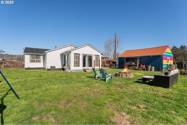 back of house featuring fence, an outdoor fire pit, central AC unit, a lawn, and an outdoor structure