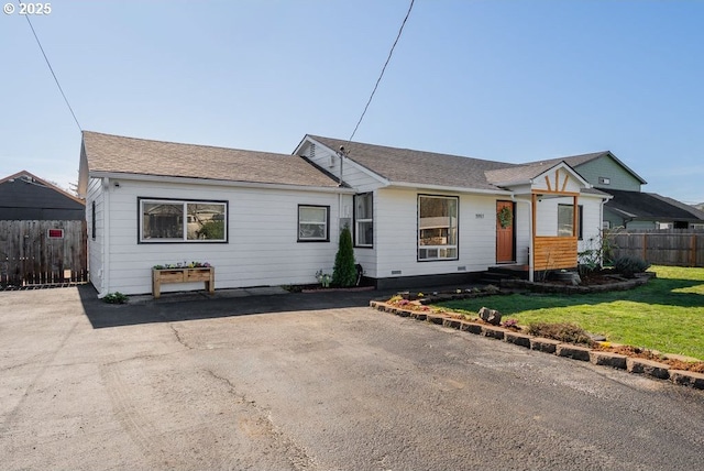 ranch-style home with a shingled roof, a front yard, and fence