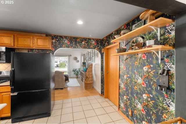 kitchen featuring light tile patterned floors, wallpapered walls, arched walkways, freestanding refrigerator, and stainless steel microwave