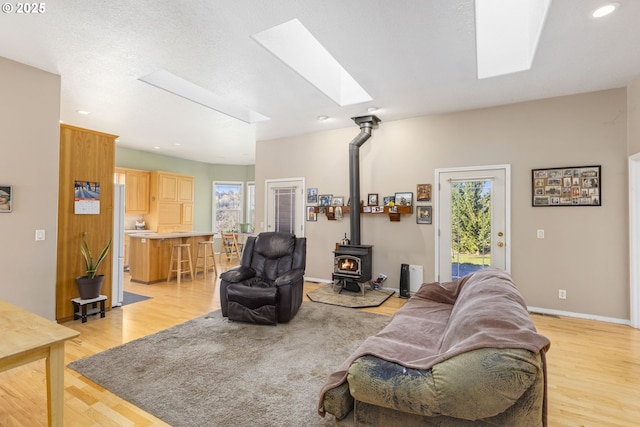 living room with a skylight, a wood stove, a wealth of natural light, and light hardwood / wood-style flooring